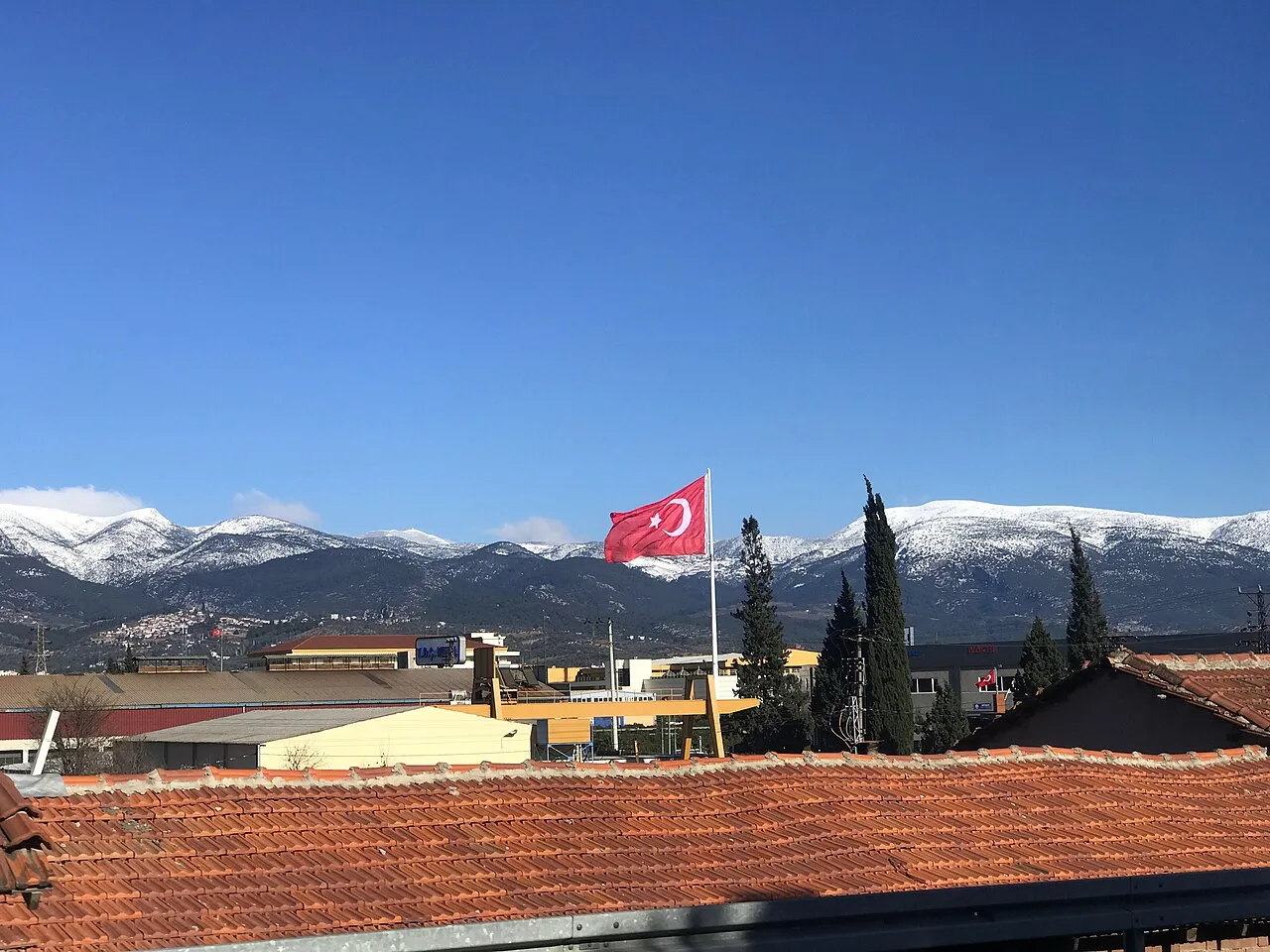 Uitzicht over daken van het district Kemalpaşa in İzmir, Turkije, met besneeuwde bergen op de achtergrond.